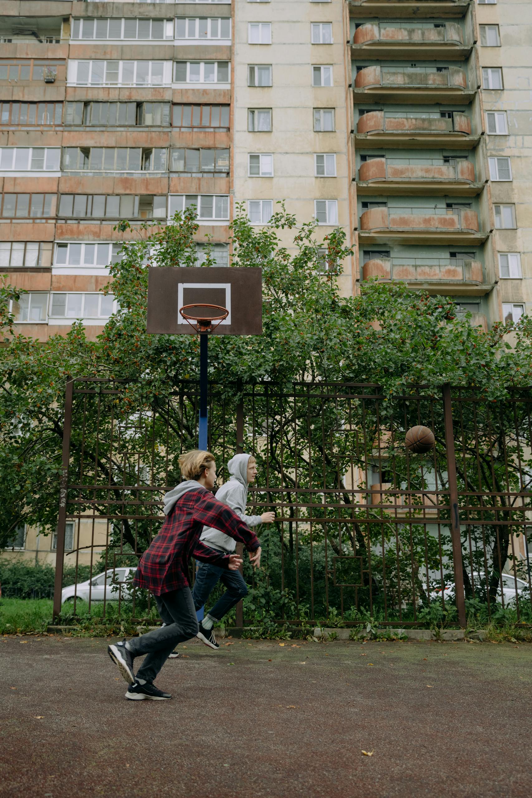 Two friends playing basketball outdoors in front of a residential building.