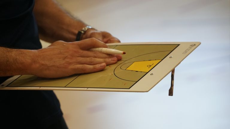 Close-up of a coach using a basketball tactics board to plan game strategy indoors.