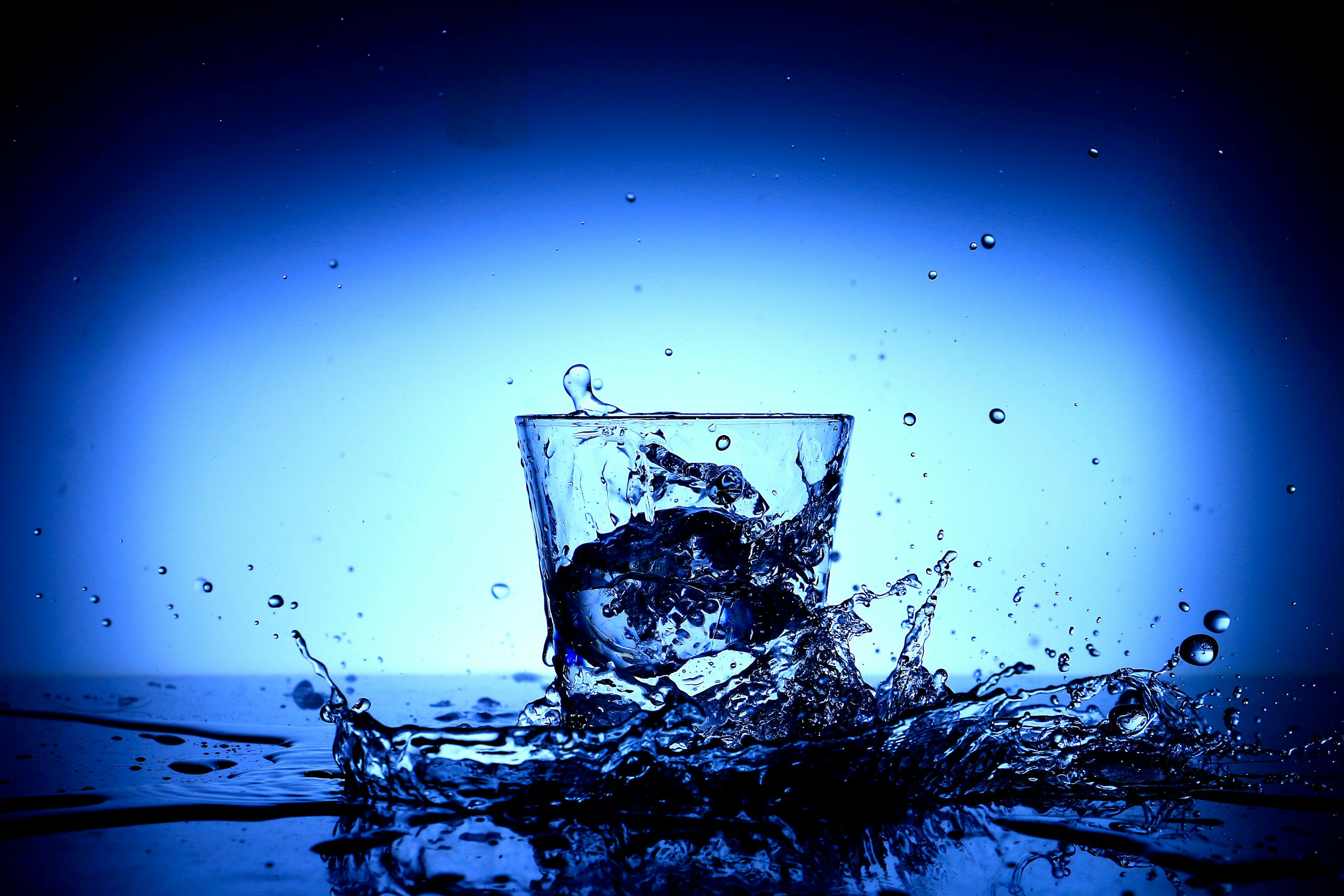 Vibrant close-up of water splashing in a glass, capturing dynamic motion and reflections.