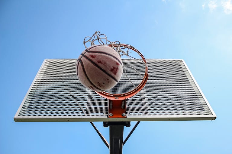 A low-angle shot of a basketball making its way through the hoop against a clear blue sky.