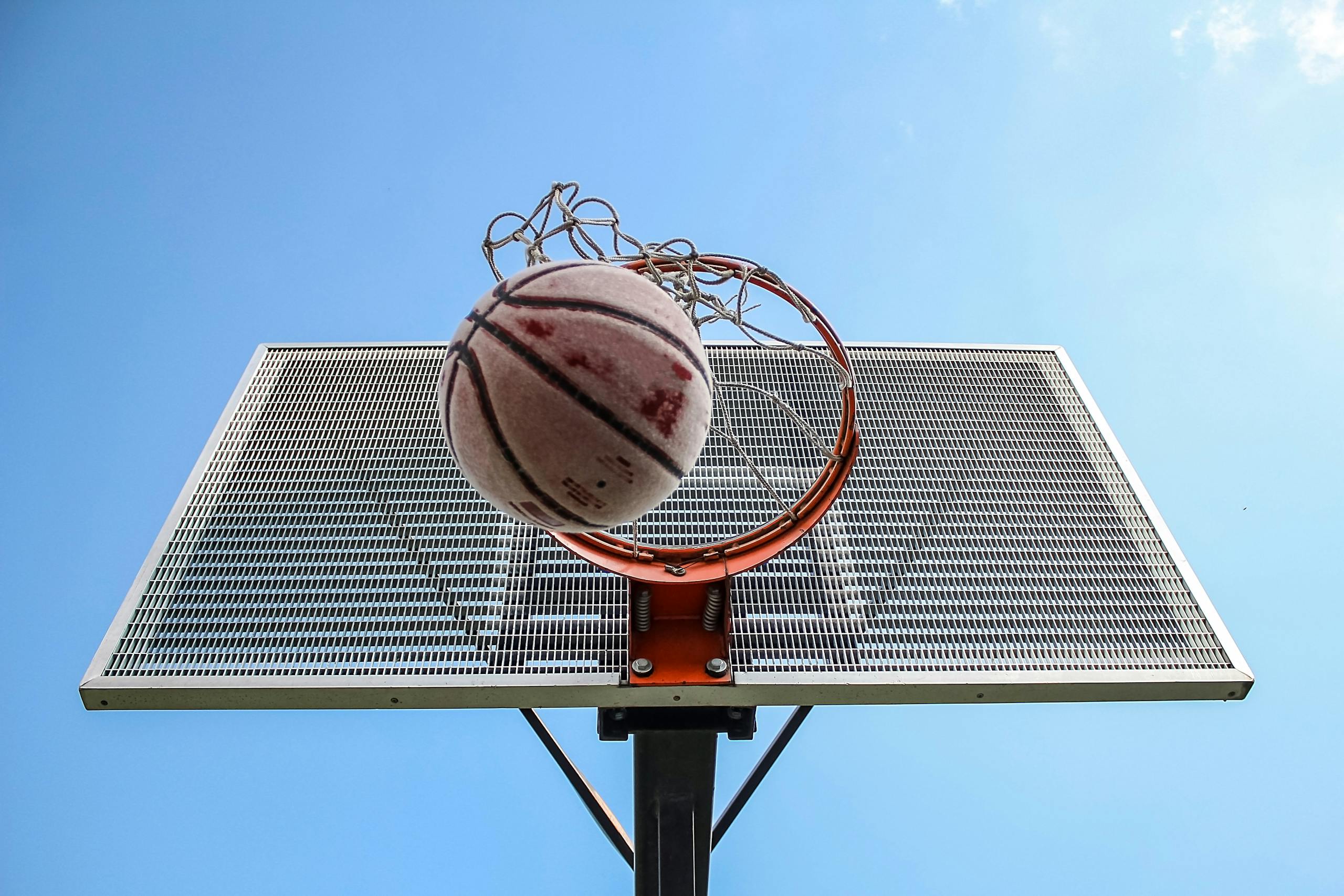 A low-angle shot of a basketball making its way through the hoop against a clear blue sky.