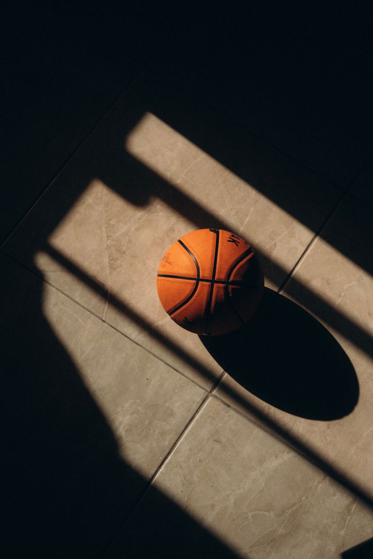 A basketball casts a shadow in sunlight, creating geometric patterns on a tiled floor.
